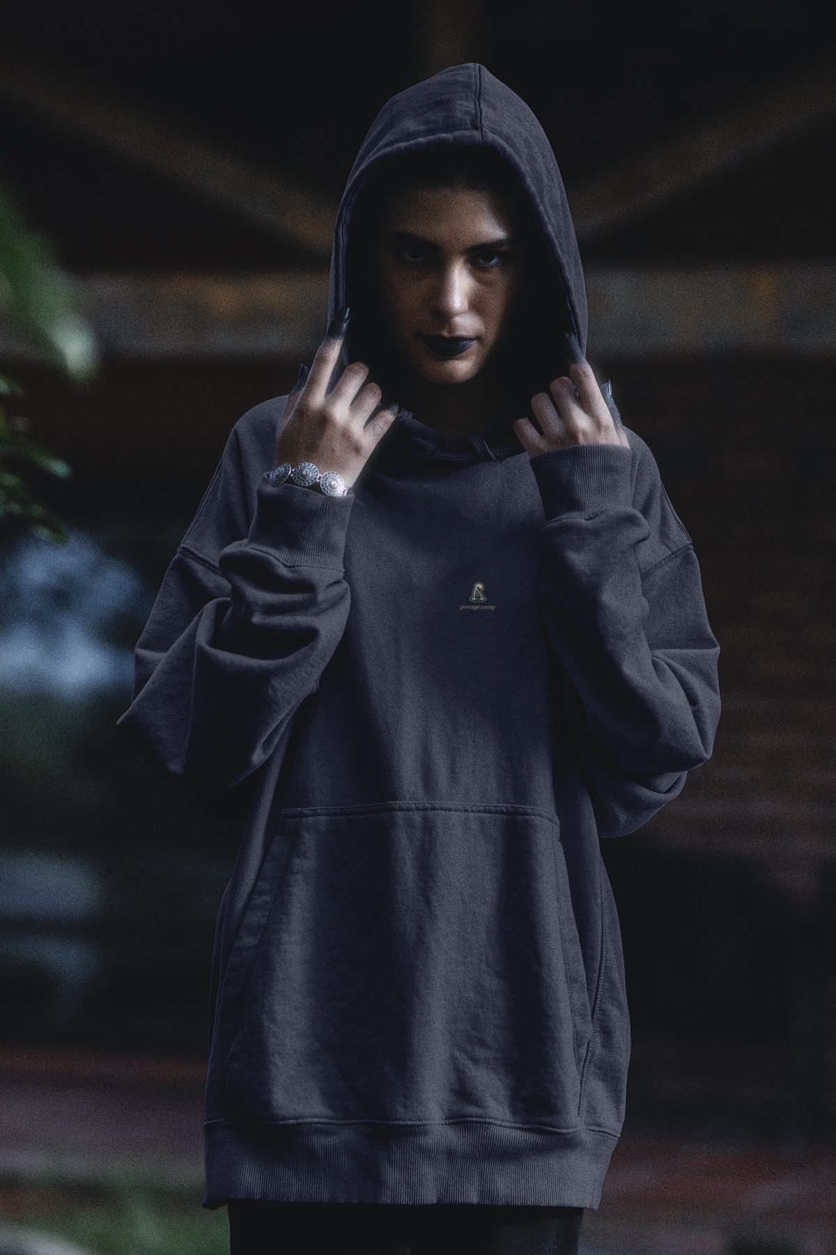 Small Hours Midweight Hoodie in Classic Navy, worn by a woman in a dark forest, with the Small Hours logo and portage.camp on the chest. Digital product mockup.