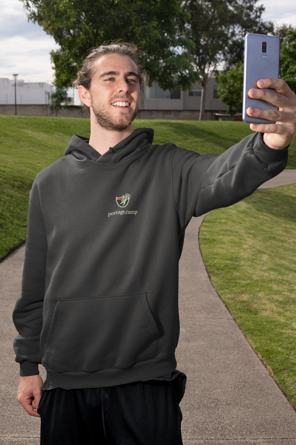 Seen Briefly Heavyweight Hoodie in Black, worn by a man taking a selfie on a city street, with the Seen Briefly logo and portage.camp on the left chest. Digital product mockup.