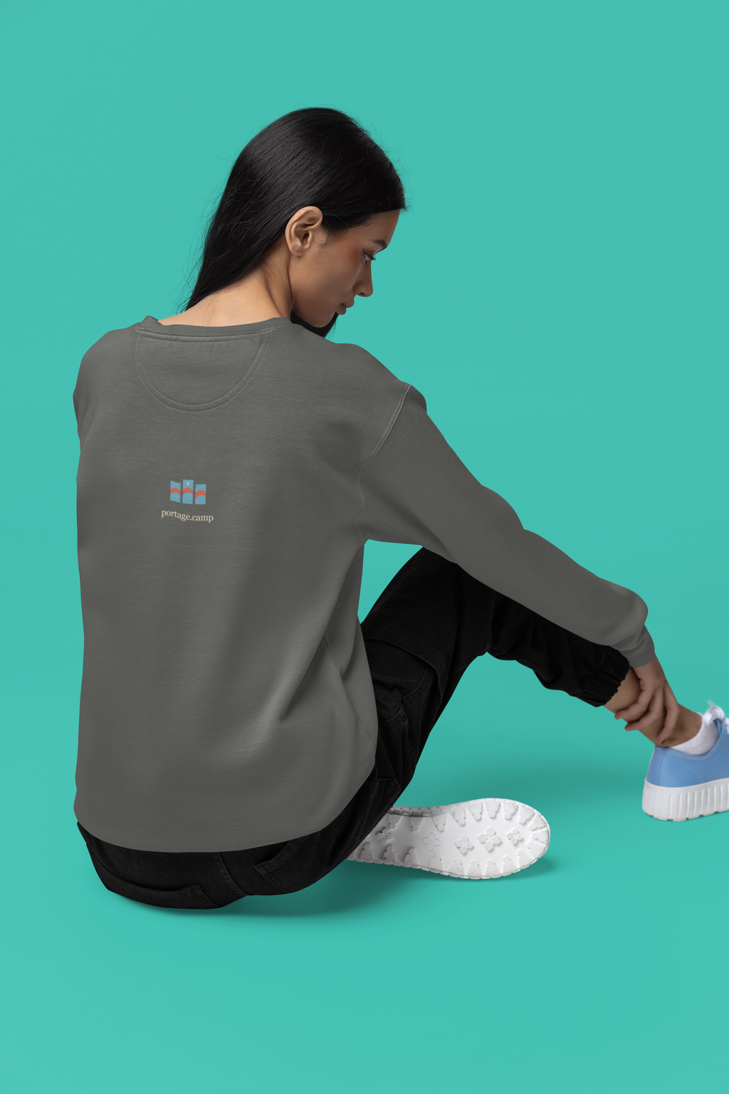 Stay for the Sky Garment-Dyed Crewneck (Front Print) in Pepper, worn by a woman seen from behind seated on a studio floor, showing the portage.camp emblem at the upper back. Digital product mockup.