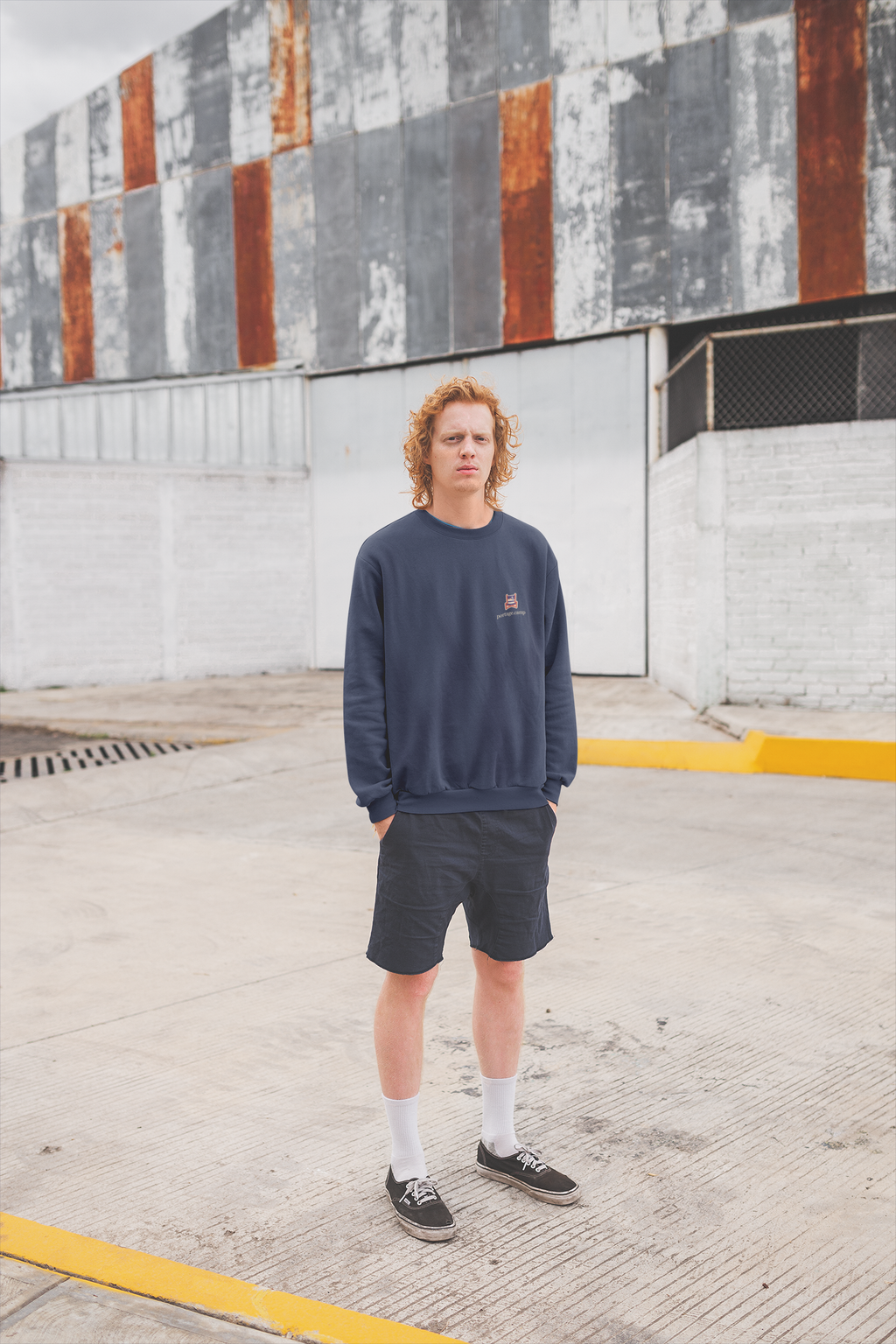 Edge of Evening Garment-Dyed Crewneck in True Navy, worn by a man against a plain wall, with the Edge of Evening logo and portage.camp on the chest. Digital product mockup.