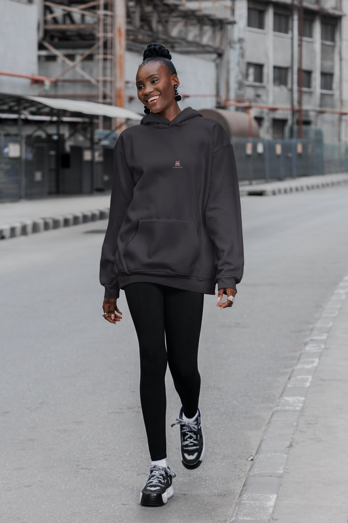 Edge of Evening Midweight Hoodie in Black, worn by a woman walking down a city street, with the Edge of Evening logo and portage.camp on the chest. Digital product mockup.