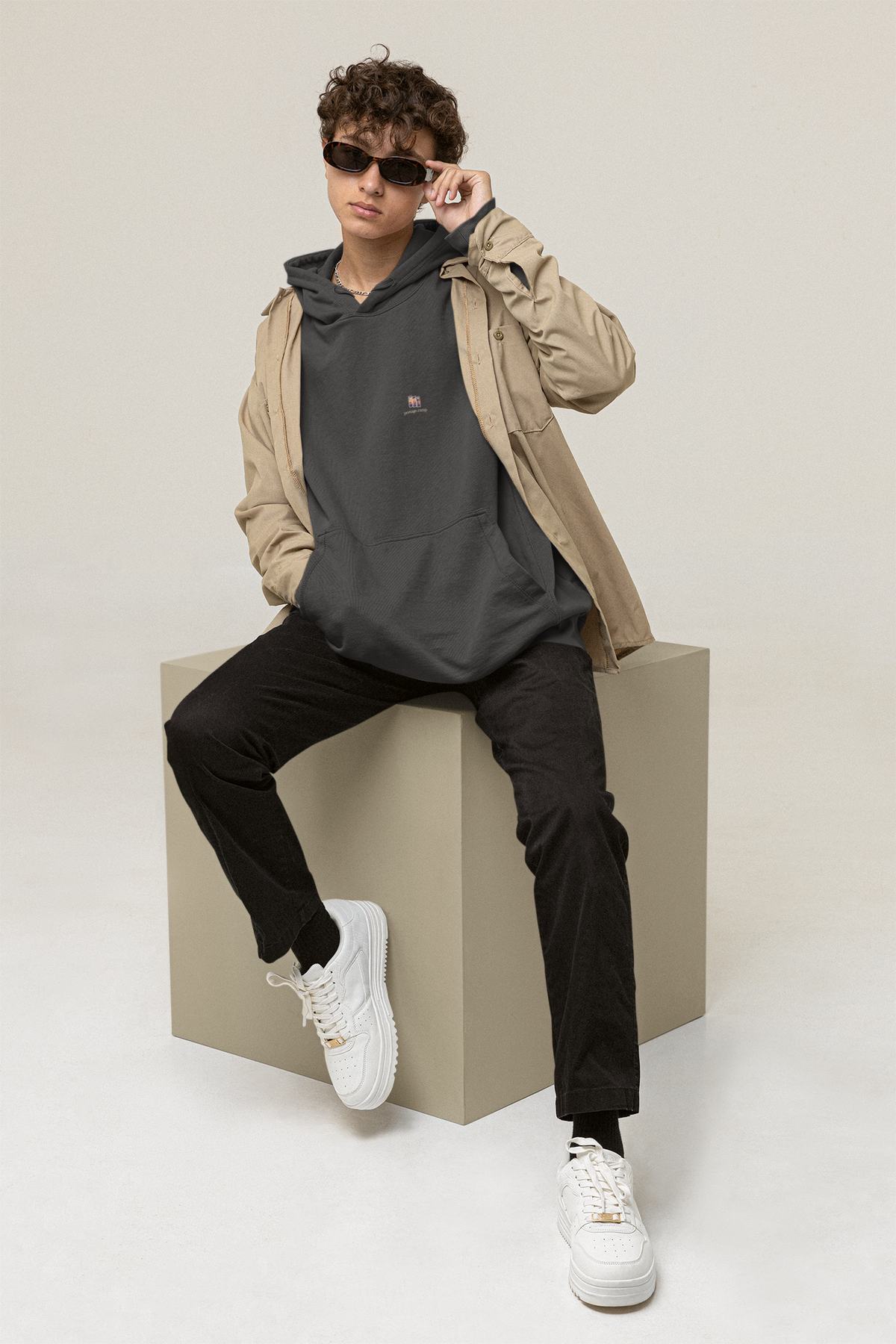 Stay for the Sky Heavyweight Hoodie in Black, worn by a man seated on a block in a studio, with the Stay for the Sky logo and portage.camp on the left chest. Digital product mockup.