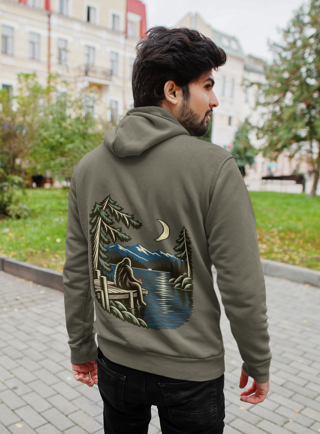 Quiet Hours Heavyweight Hoodie in Olive, worn by a man seen from behind on a quiet city street, showing the large print on the back. Digital product mockup.