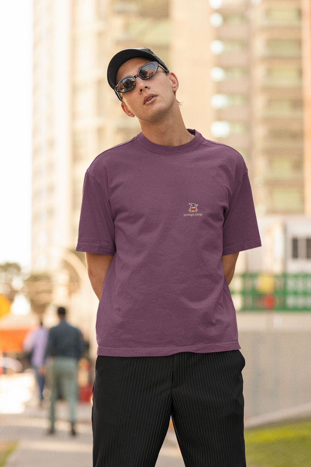 Cloud Ferry Garment-Dyed Tee in Berry, worn by a man in a cap and sunglasses on a city street, with the Cloud Ferry logo and portage.camp on the chest. Digital product mockup.