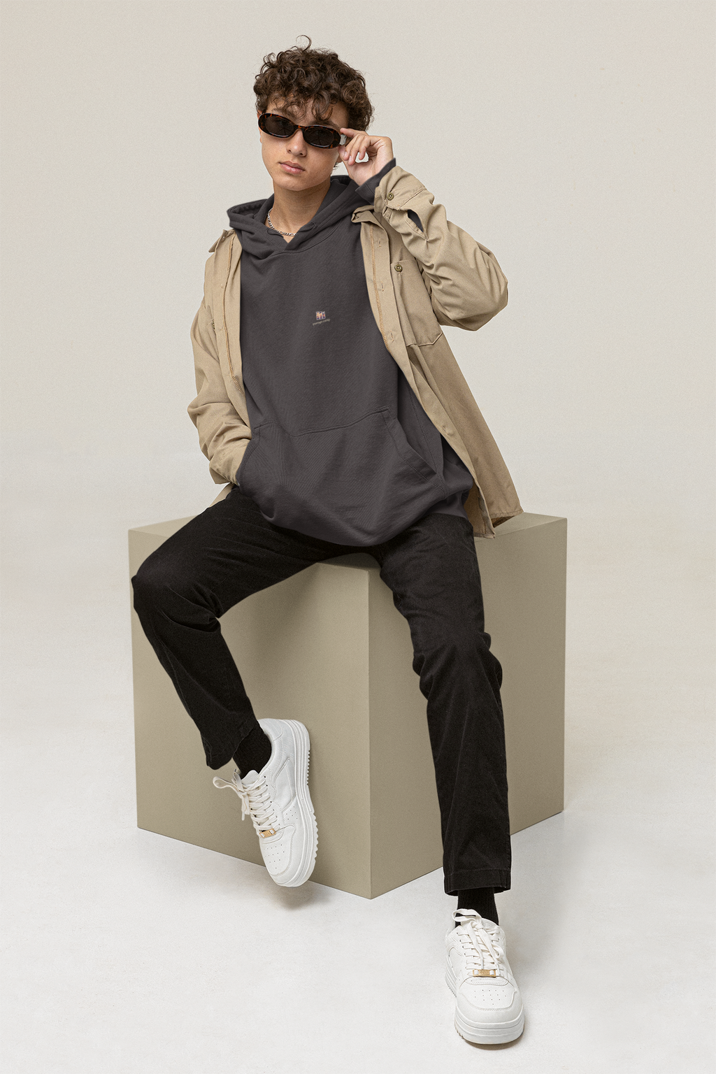 Stay for the Sky Midweight Hoodie in Black, worn by a man seated on a block in a studio, with the Stay for the Sky logo and portage.camp on the chest. Digital product mockup.