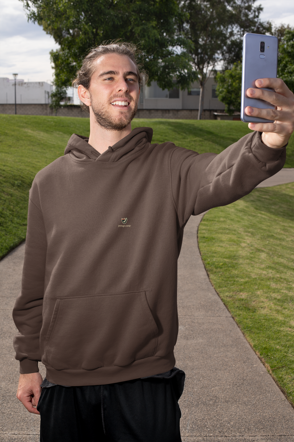 Seen Briefly Heavyweight Hoodie in Brown, worn by a man taking a selfie on a city street, with the Seen Briefly logo and portage.camp on the left chest. Digital product mockup.