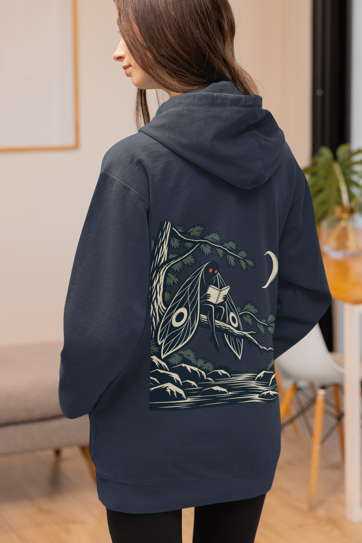 Night Library Zip Hoodie in Navy, worn by a woman seen from behind at home, showing the large print on the back. Digital product mockup.