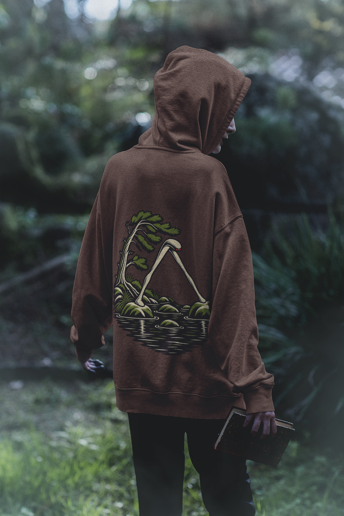 Small Hours Heavyweight Hoodie in Brown, worn by a woman seen from behind in a dark forest, showing the large print on the back. Digital product mockup.