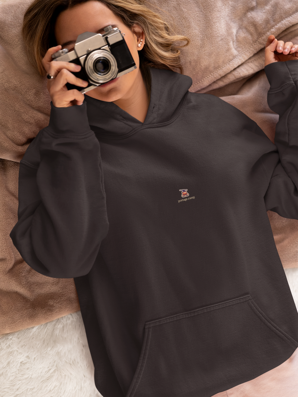 Cloud Ferry Midweight Hoodie in Black, worn by a woman in bed with a film camera, with the Cloud Ferry logo and portage.camp on the chest. Digital product mockup.