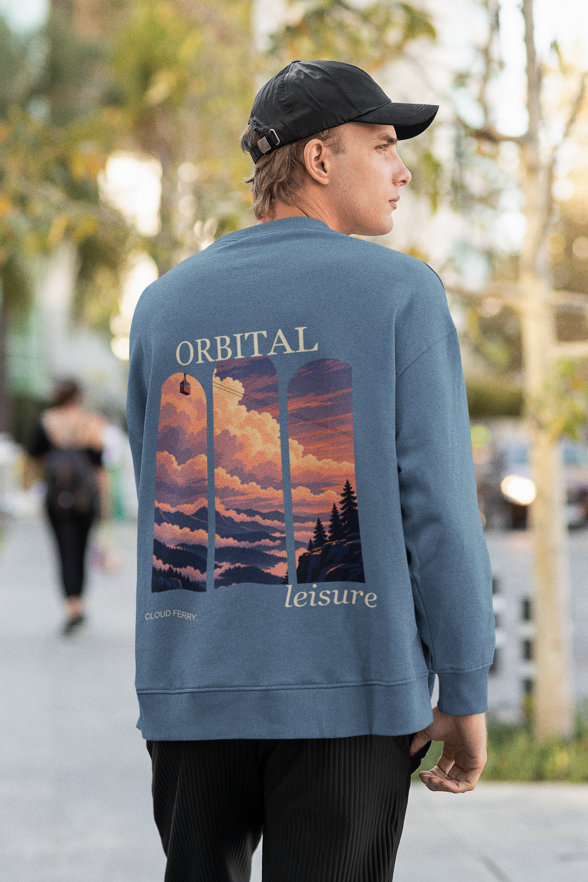 Cloud Ferry Garment-Dyed Crewneck in Blue Jean, worn by a man seen from behind walking down a city street, showing the large print on the back. Digital product mockup.