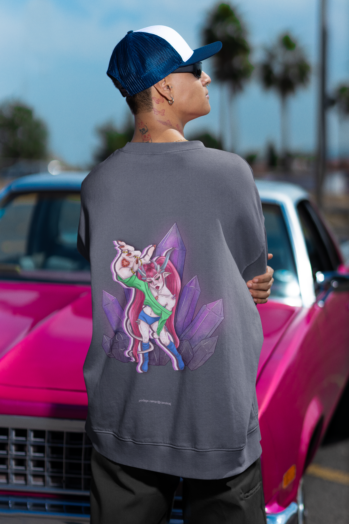 Amethyst After Hours Garment-Dyed Crewneck in Denim, worn by a man seen from behind by a pink classic car, showing the large print on the back. Digital product mockup.