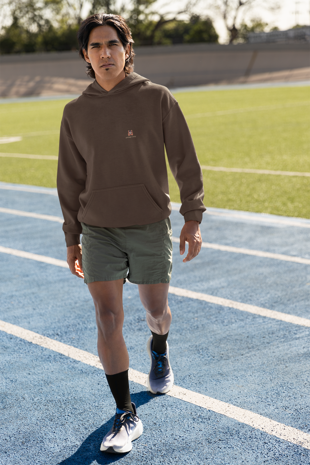 Edge of Evening Heavyweight Hoodie in Brown, worn by a man on a running track, with the Edge of Evening logo and portage.camp on the left chest. Digital product mockup.