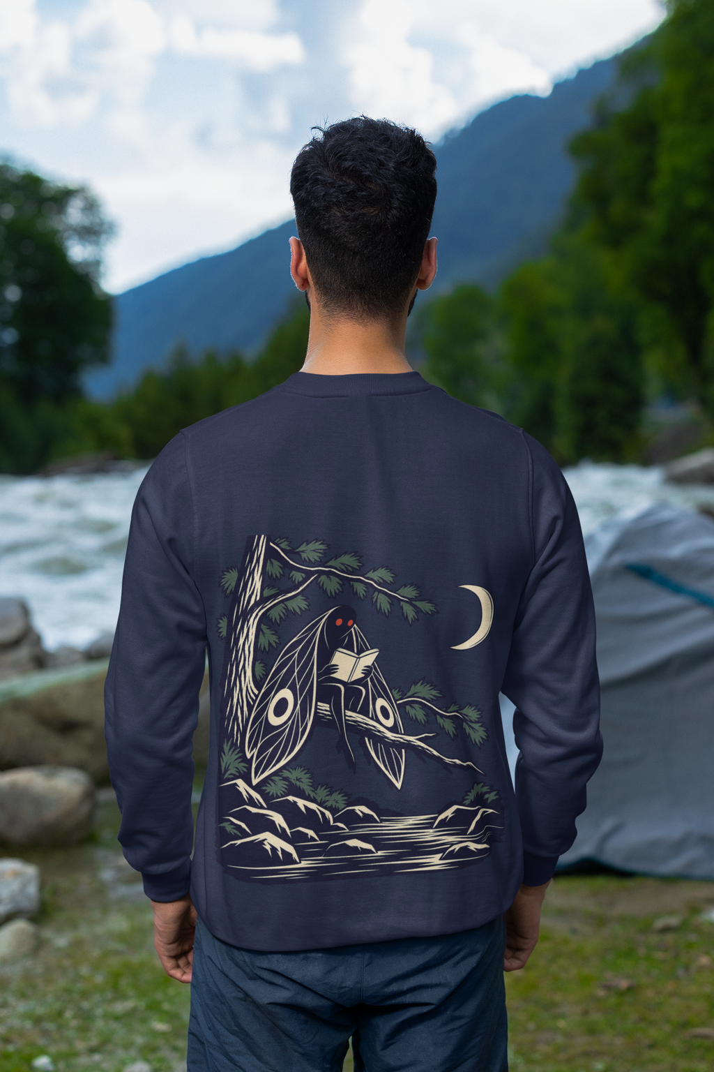 Night Library Garment-Dyed Crewneck in True Navy, worn by a man seen from behind looking out over a mountain valley, showing the large print on the back. Digital product mockup.