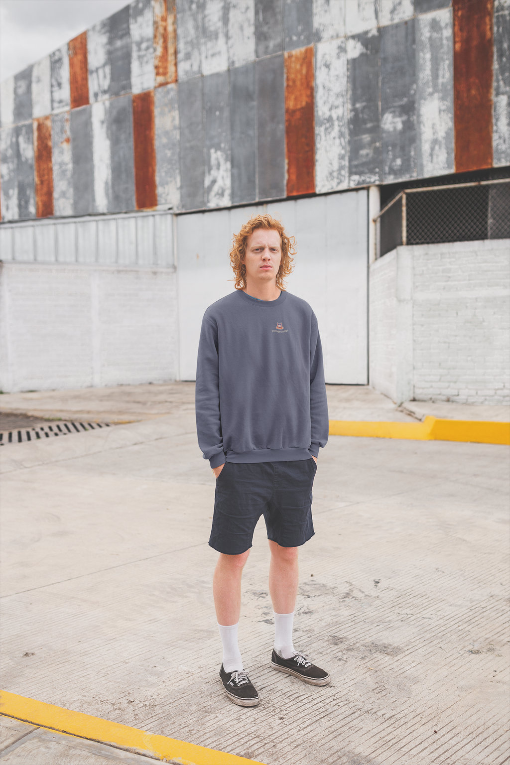 Edge of Evening Garment-Dyed Crewneck in Denim, worn by a man against a plain wall, with the Edge of Evening logo and portage.camp on the chest. Digital product mockup.