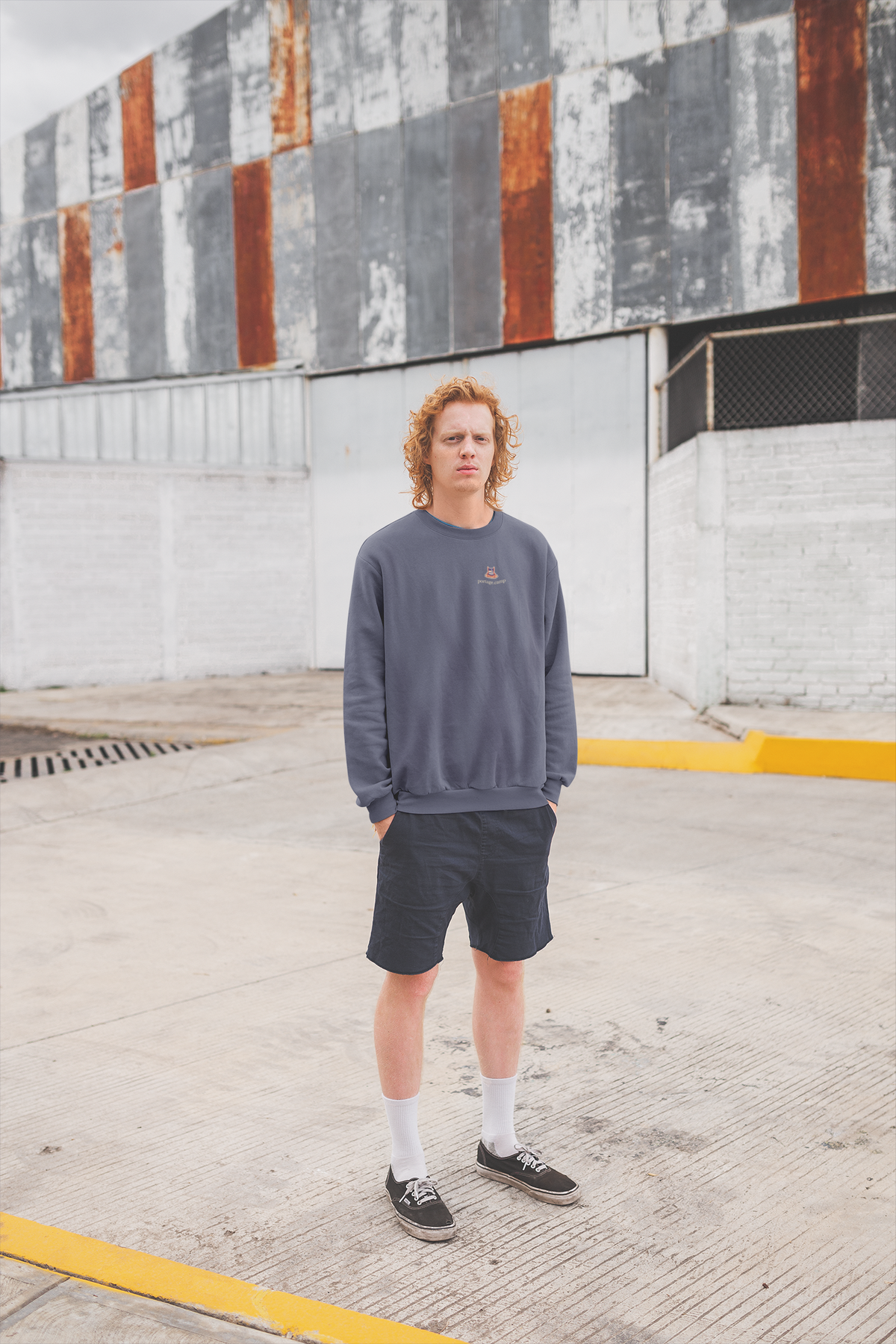 Edge of Evening Garment-Dyed Crewneck in Denim, worn by a man against a plain wall, with the Edge of Evening logo and portage.camp on the chest. Digital product mockup.