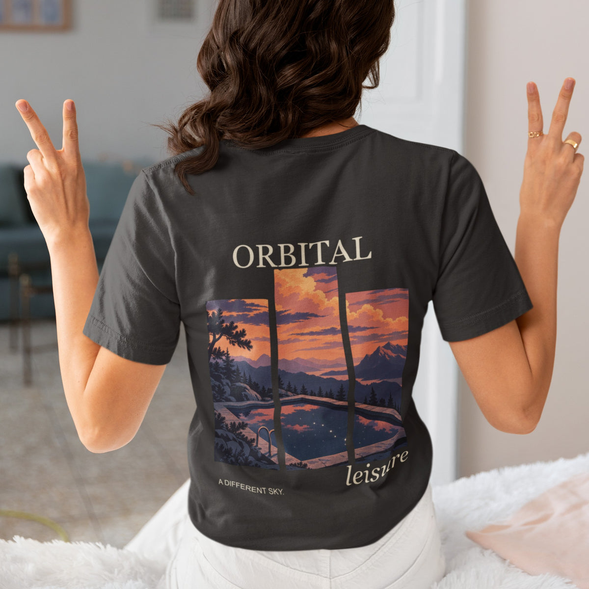 A Different Sky Garment-Dyed Tee in Black, worn by a woman seen from behind making peace signs, showing the large print on the back. Digital product mockup.