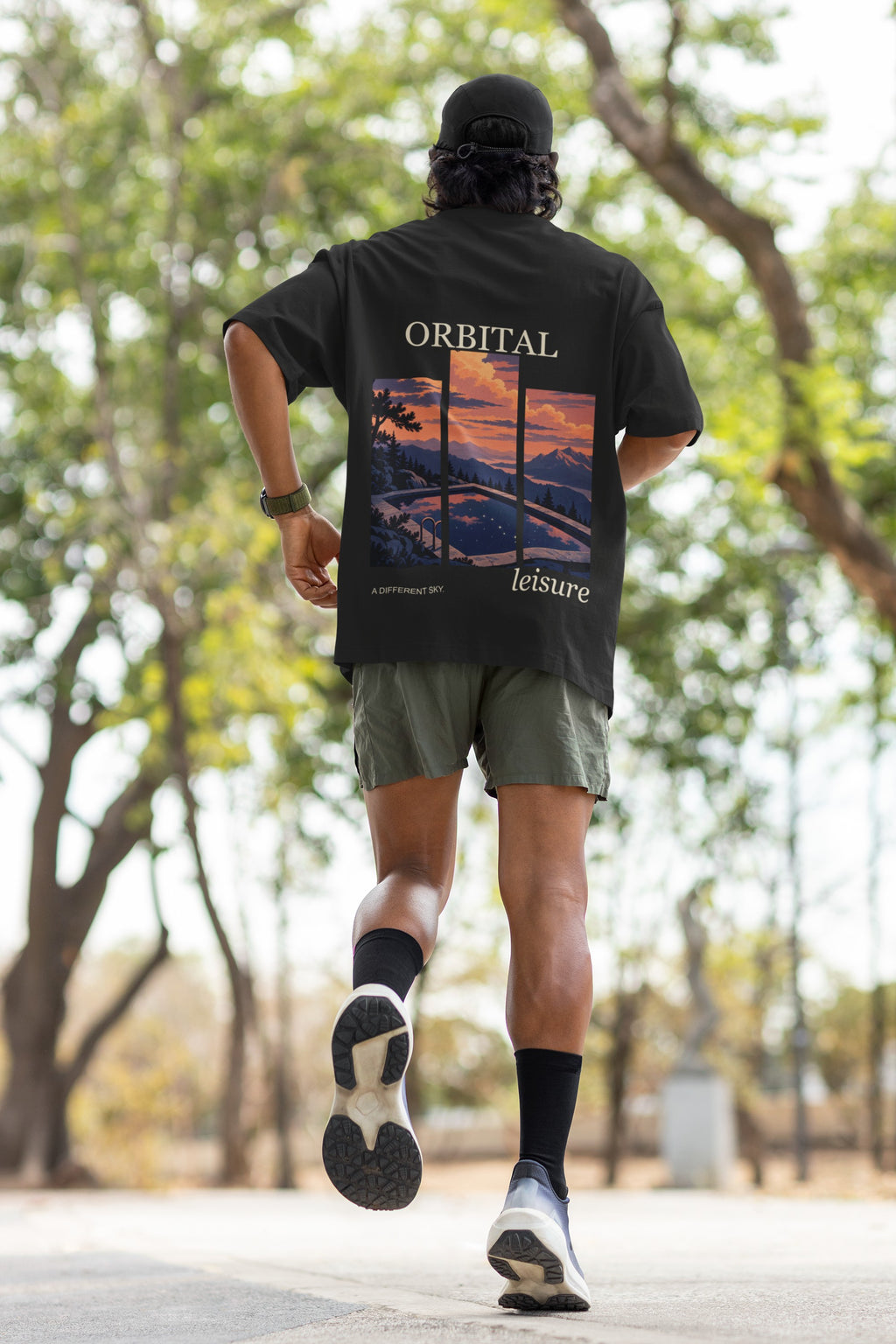 A Different Sky Garment-Dyed Tee in Black, worn by a man seen from behind jogging through a park, showing the large print on the back. Digital product mockup.
