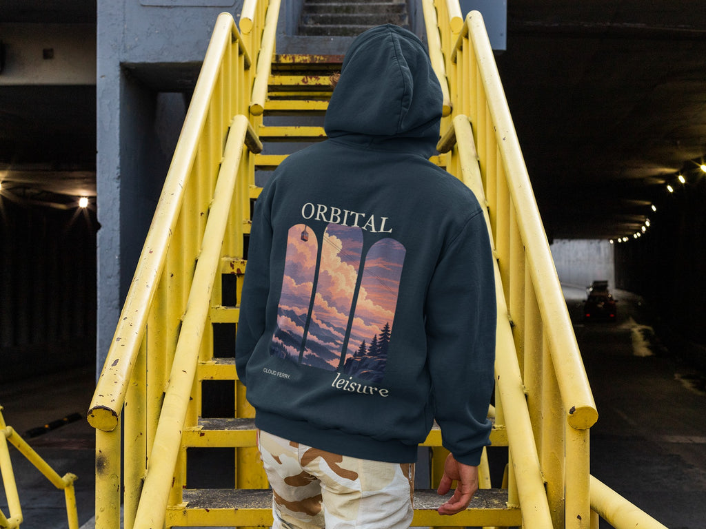 Cloud Ferry Midweight Hoodie in Classic Navy, worn by a man seen from behind climbing a yellow metal staircase, showing the large print on the back. Digital product mockup.