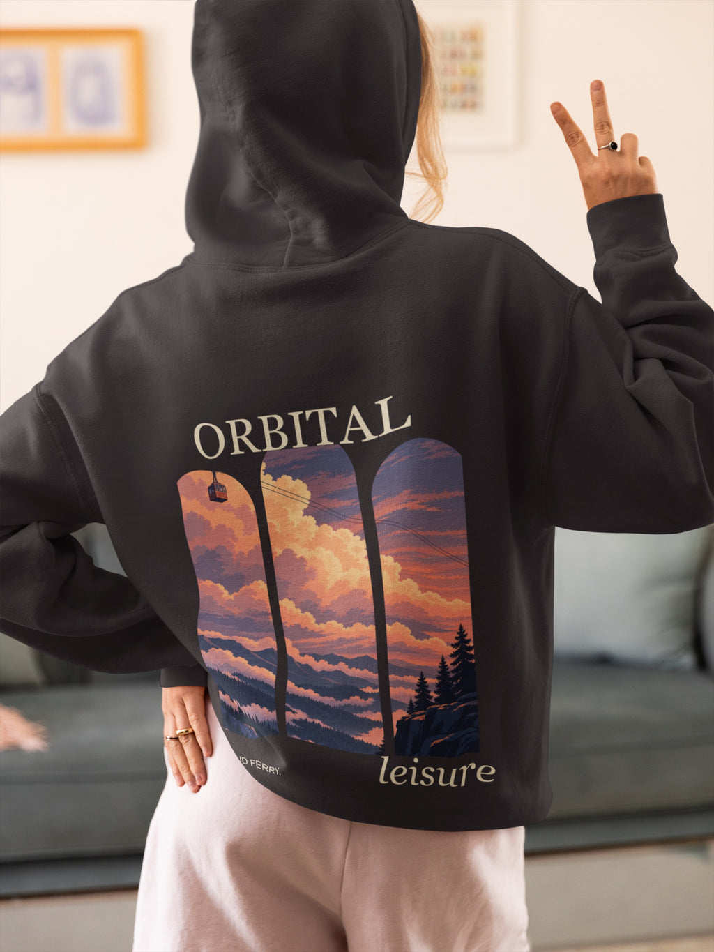 Cloud Ferry Midweight Hoodie in Black, worn by a woman seen from behind at home, making a peace sign, showing the large print on the back. Digital product mockup.