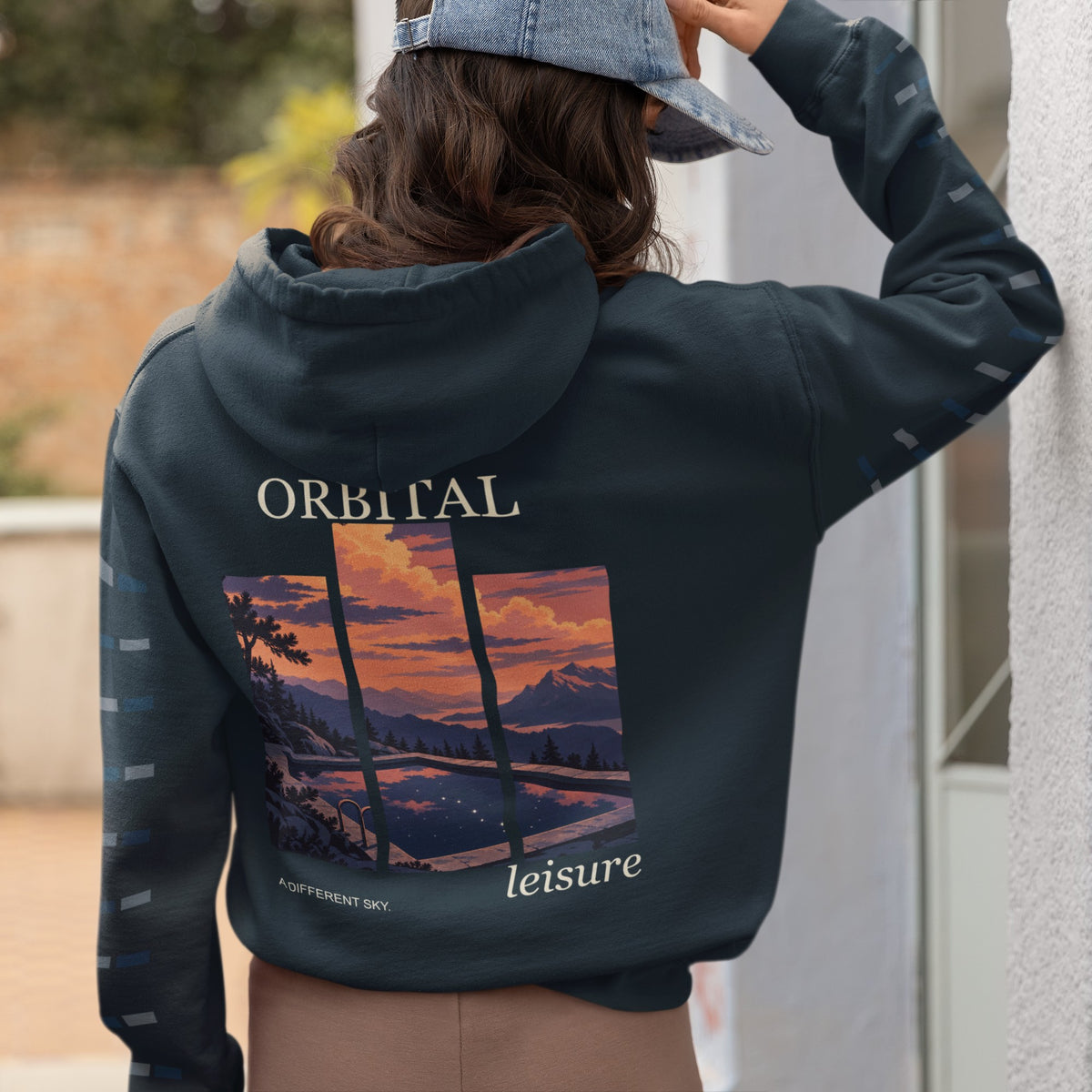 A Different Sky Midweight Hoodie in Classic Navy, worn by a woman seen from behind at home, showing the large print on the back. Digital product mockup.