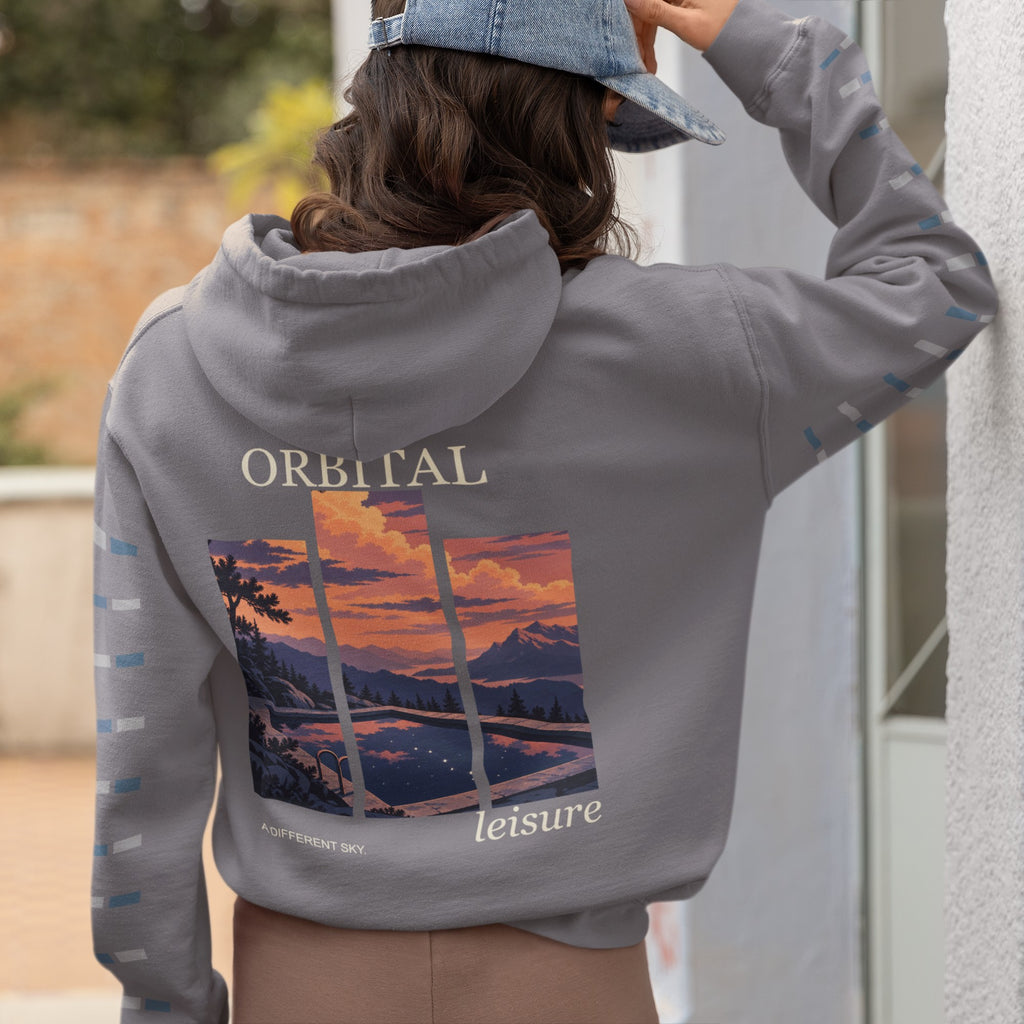 A Different Sky Midweight Hoodie in Charcoal, worn by a woman seen from behind at home, showing the large print on the back. Digital product mockup.