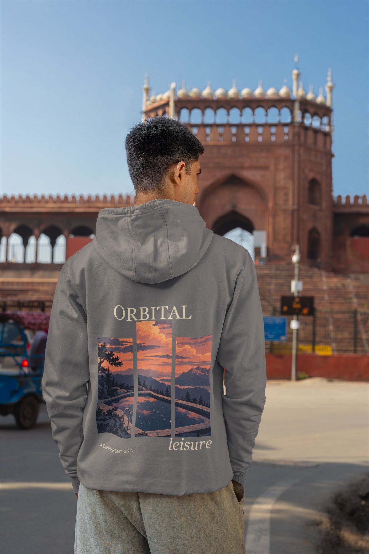 A Different Sky Midweight Hoodie in Charcoal, worn by a man seen from behind on a city street, showing the large print on the back. Digital product mockup.