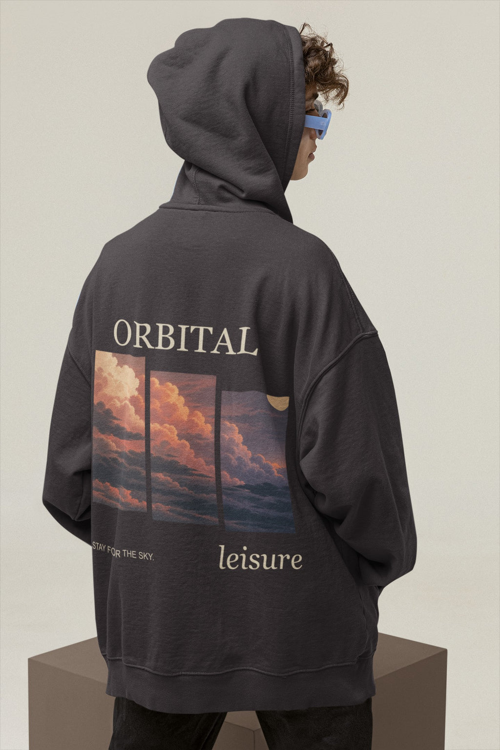 Stay for the Sky Heavyweight Hoodie in Black, worn by a man seen from behind in a studio with the hood up, showing the large print on the back. Digital product mockup.