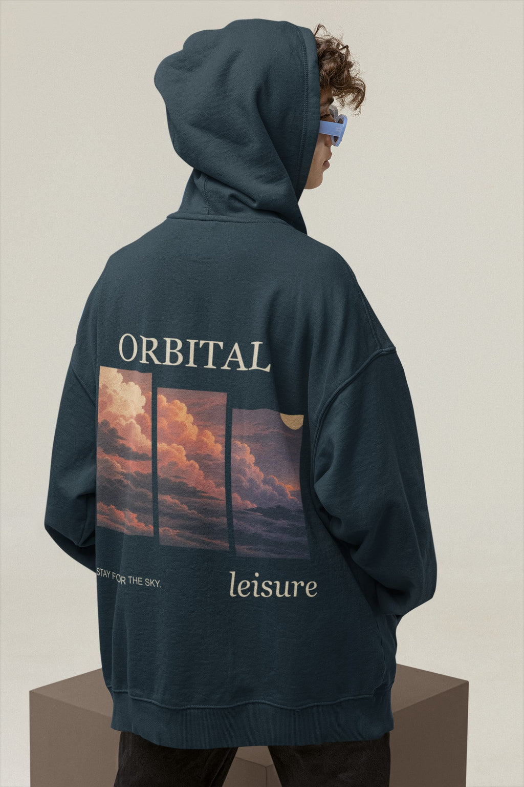 Stay for the Sky Midweight Hoodie in Classic Navy, worn by a man seen from behind in a studio with the hood up, showing the large print on the back. Digital product mockup.
