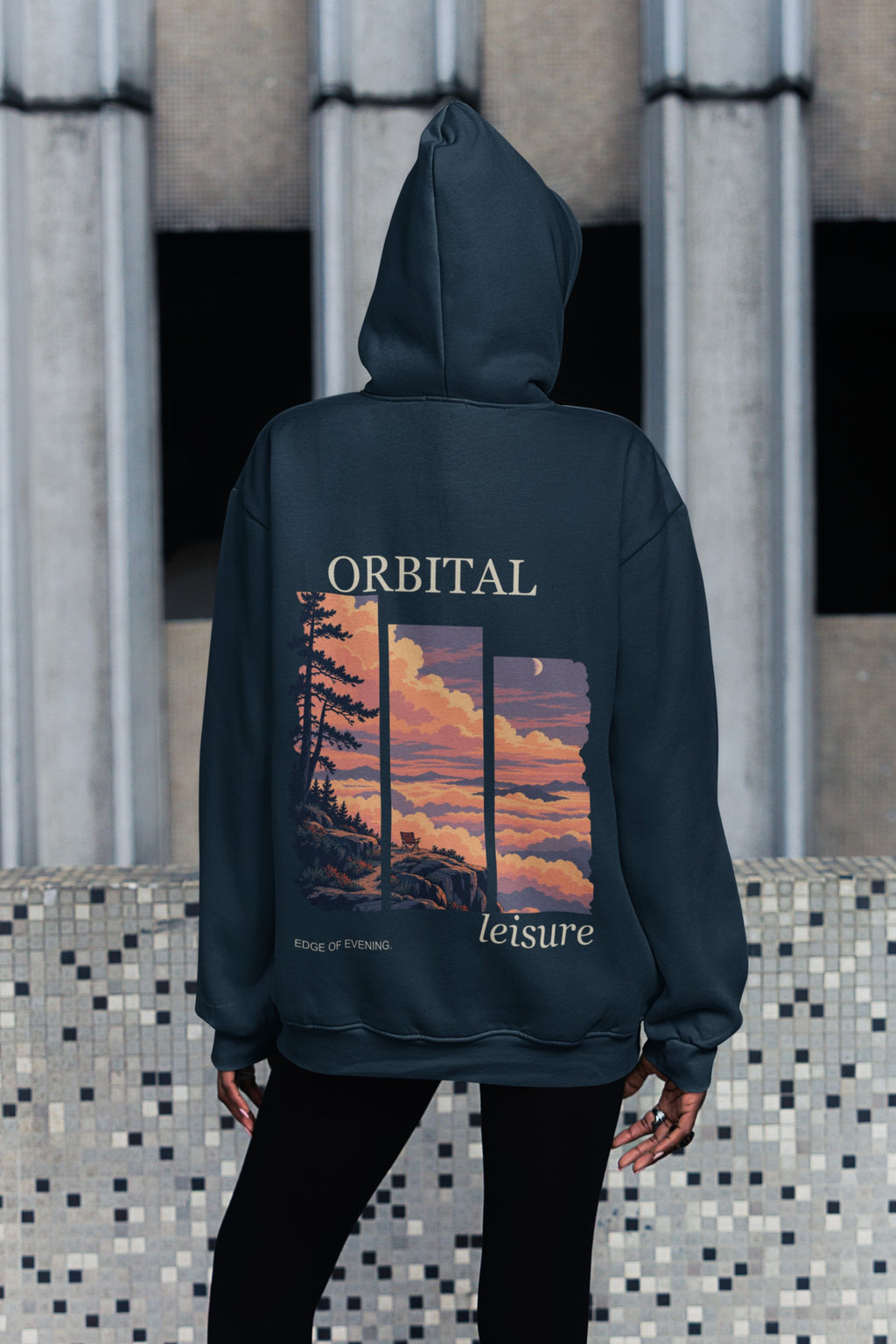 Edge of Evening Midweight Hoodie in Classic Navy, worn by a woman seen from behind on a city sidewalk, showing the large print on the back. Digital product mockup.