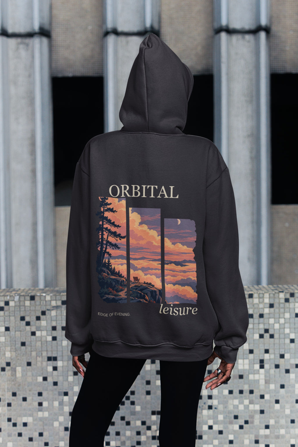 Edge of Evening Midweight Hoodie in Black, worn by a woman seen from behind on a city sidewalk, showing the large print on the back. Digital product mockup.