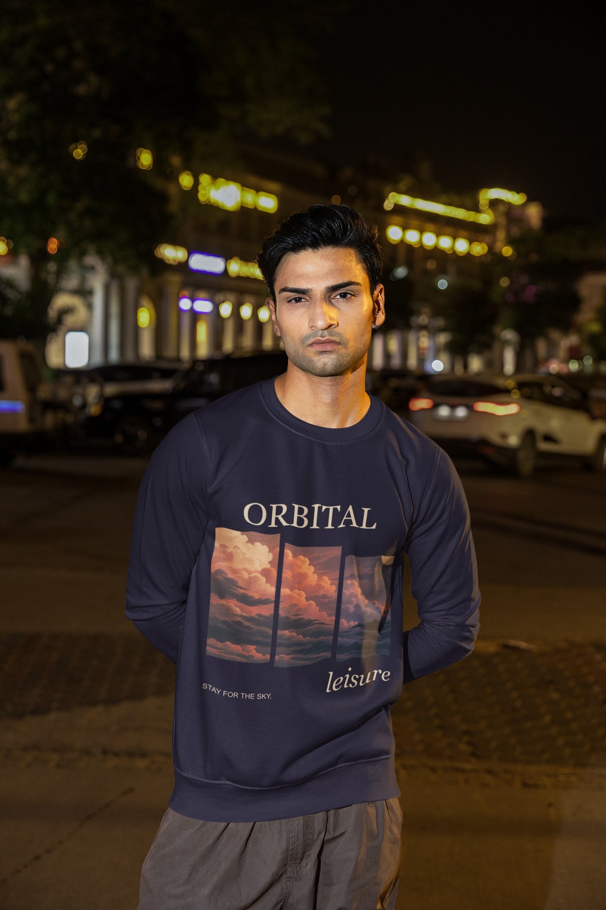Stay for the Sky Garment-Dyed Crewneck (Front Print) in True Navy, worn by a man on a city street at night, showing the large print on the front. Digital product mockup.