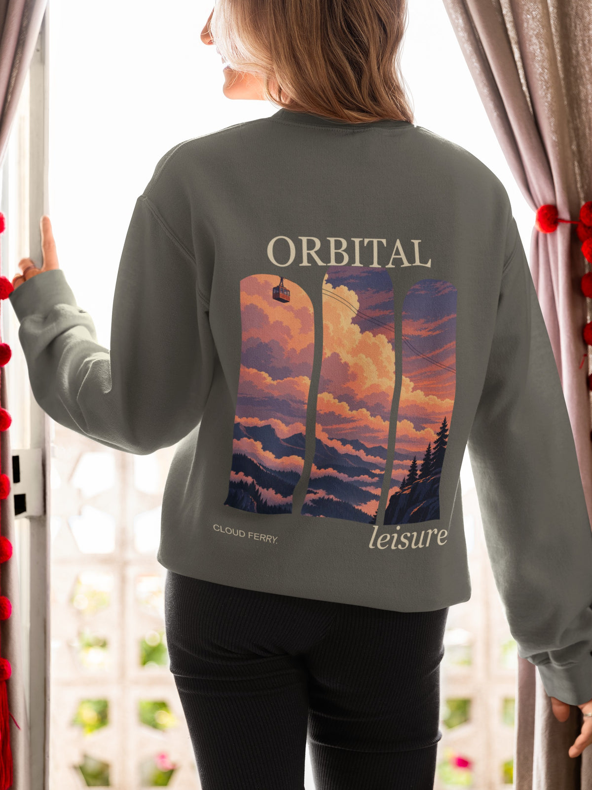 Cloud Ferry Garment-Dyed Crewneck in Pepper, worn by a woman seen from behind at an open door, showing the large print on the back. Digital product mockup.