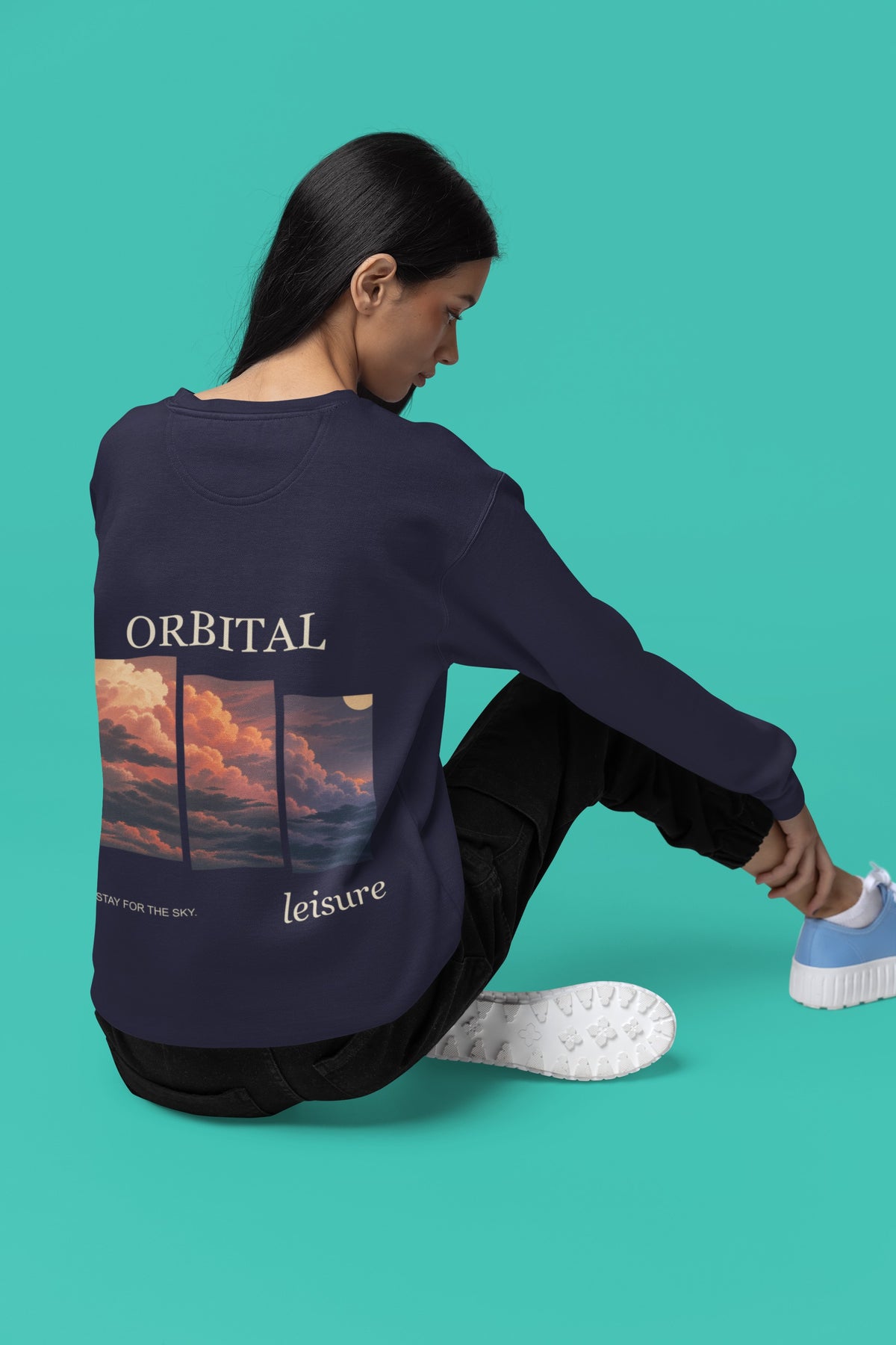 Stay for the Sky Garment-Dyed Crewneck in True Navy, worn by a woman seen from behind seated on a studio floor, showing the large print on the back. Digital product mockup.
