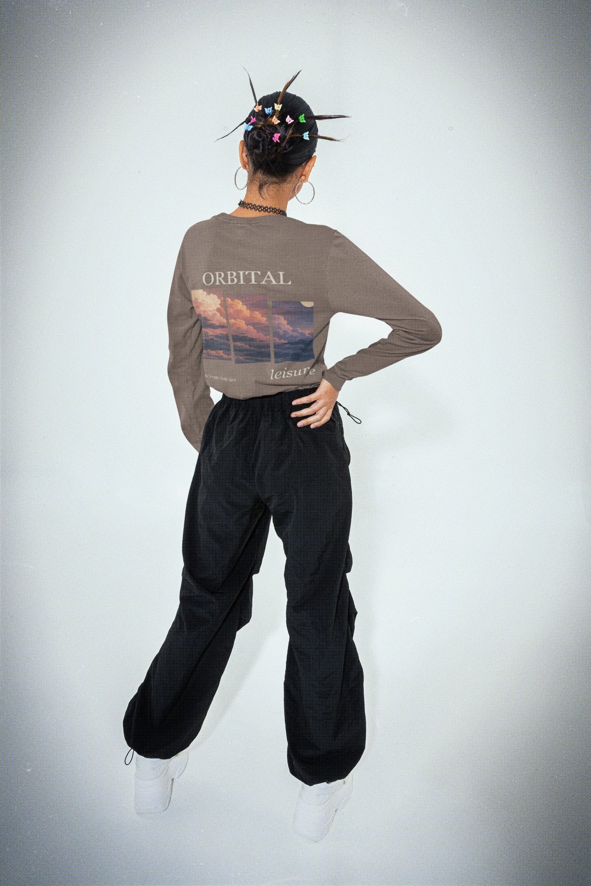 Stay for the Sky Garment-Dyed Long-Sleeve Tee in Espresso, worn by a woman seen from behind in a studio, showing the large print on the back. Digital product mockup.