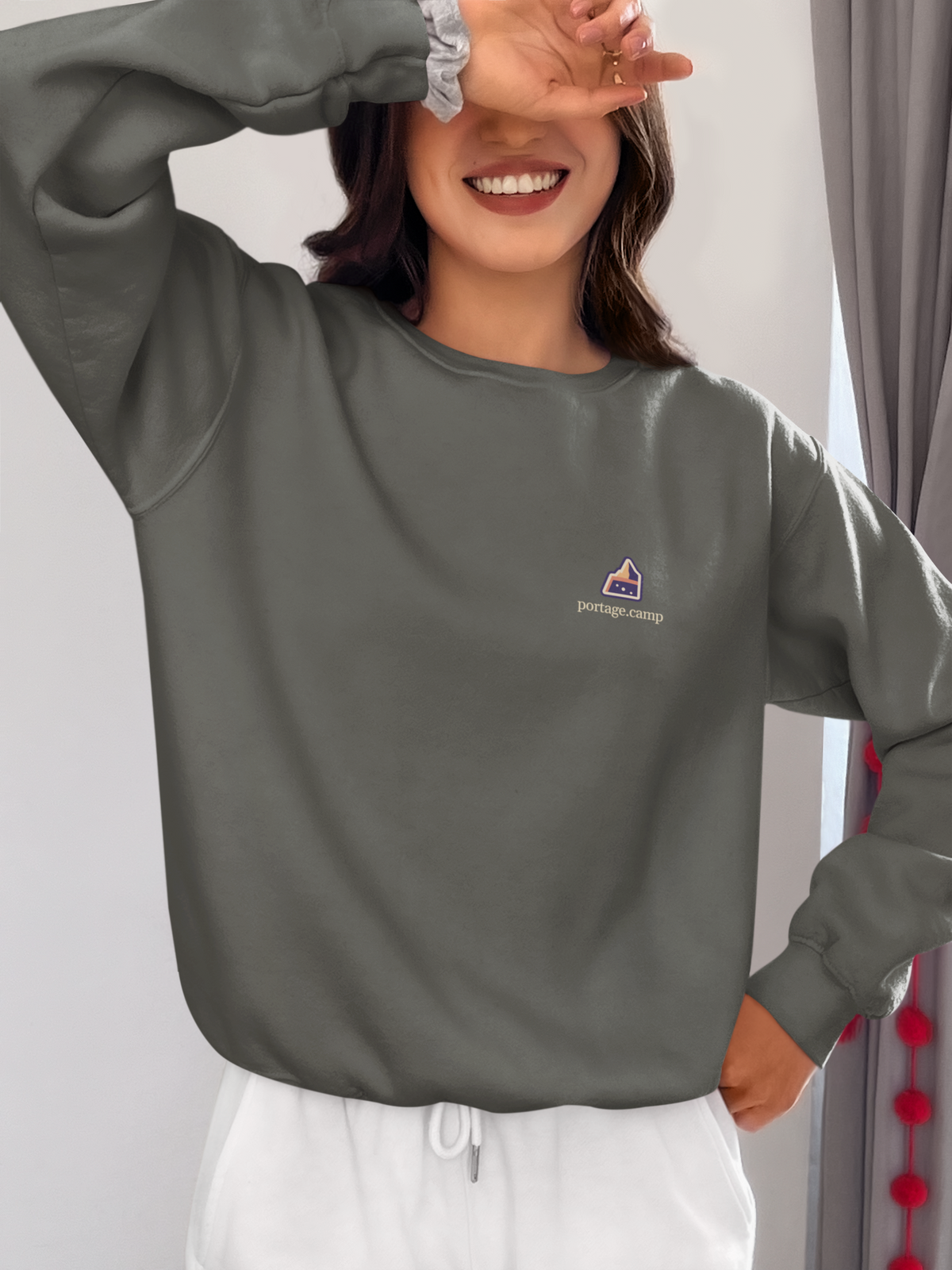 A Different Sky Garment-Dyed Crewneck in Pepper, worn by a woman at home, with the A Different Sky logo and portage.camp on the chest. Digital product mockup.