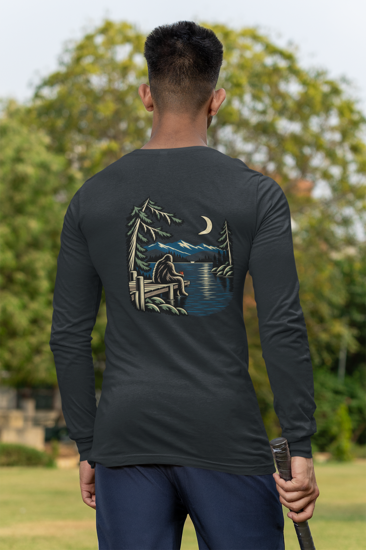 Quiet Hours Garment-Dyed Long-Sleeve Tee in Black, worn by a man seen from behind at a cricket field, showing the large print on the back. Digital product mockup.