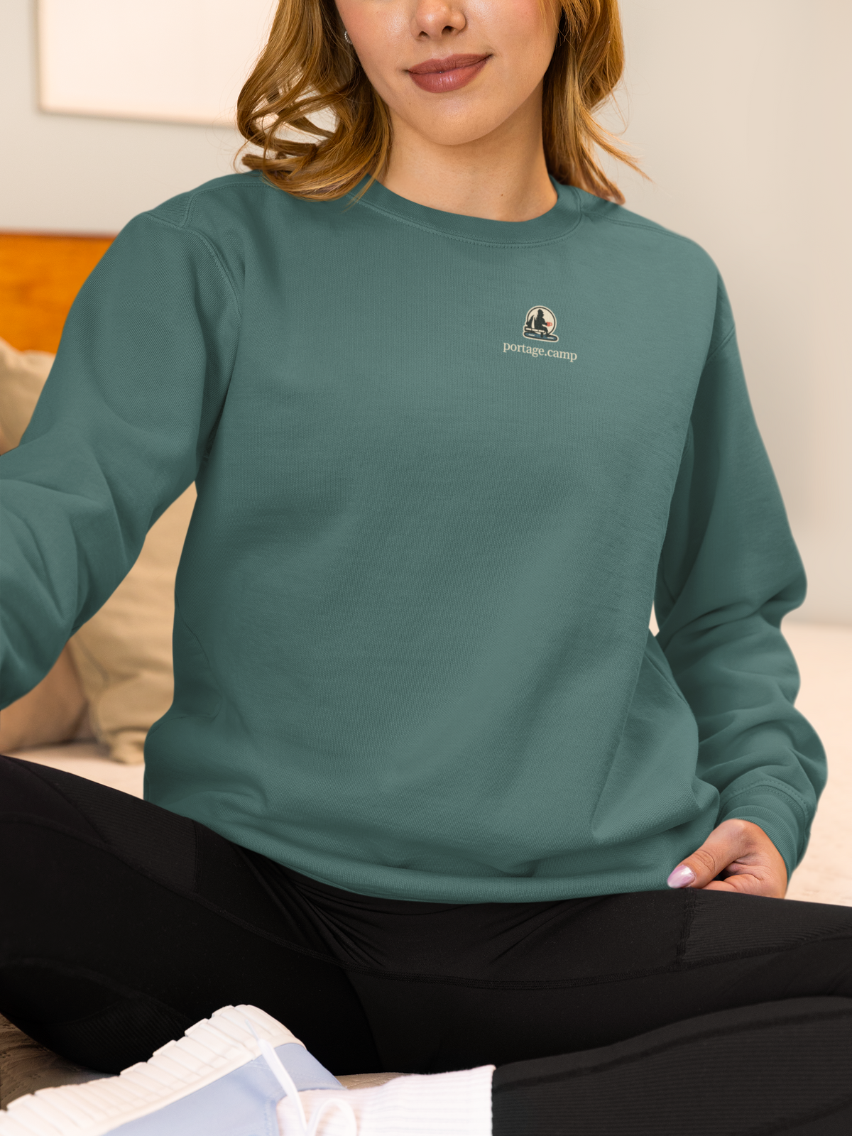 Quiet Hours Garment-Dyed Crewneck in Blue Spruce, worn by a woman at home, with the Quiet Hours logo and portage.camp on the chest. Digital product mockup.
