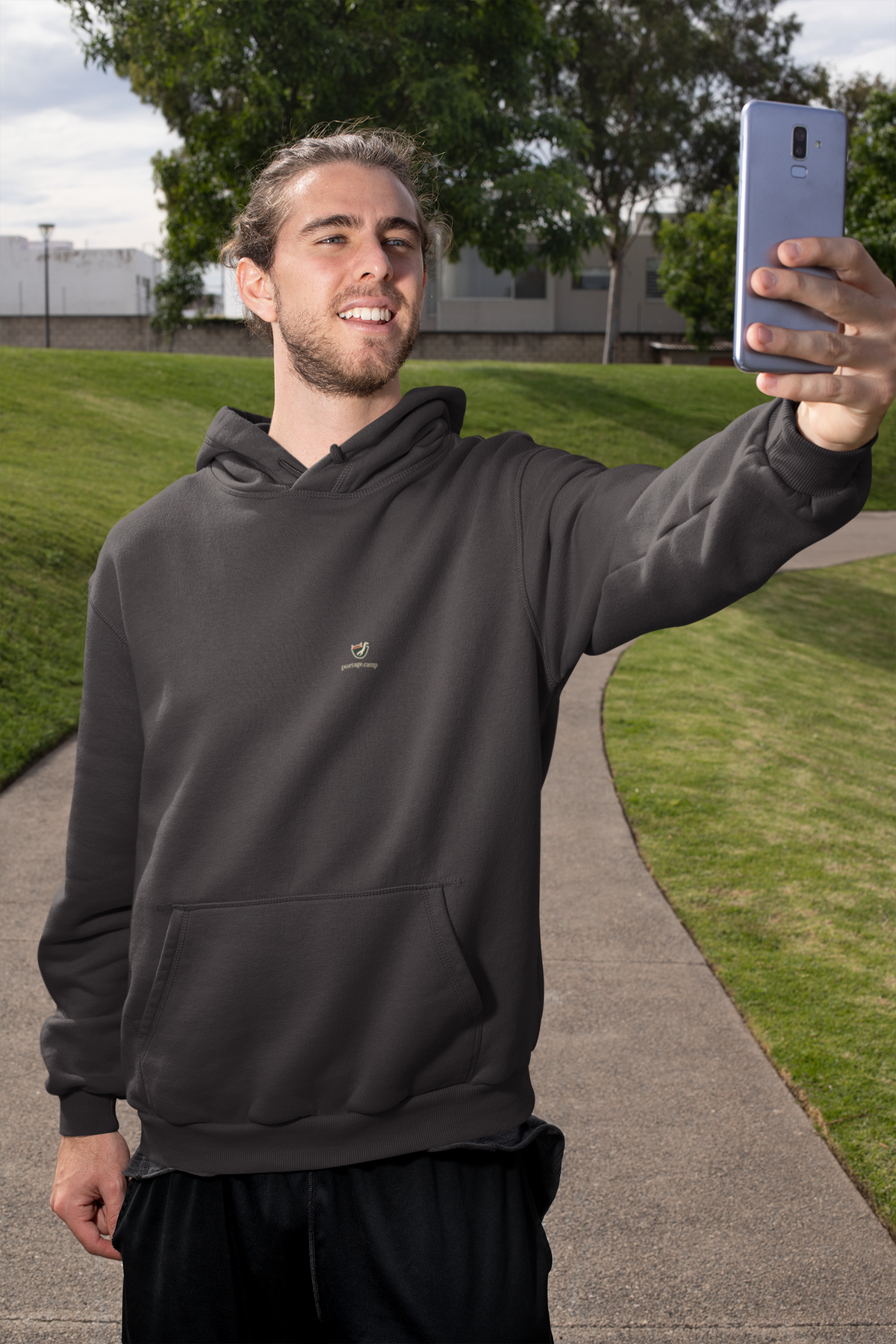 Seen Briefly Midweight Hoodie in Black, worn by a man taking a selfie on a city street, with the Seen Briefly logo and portage.camp on the chest. Digital product mockup.