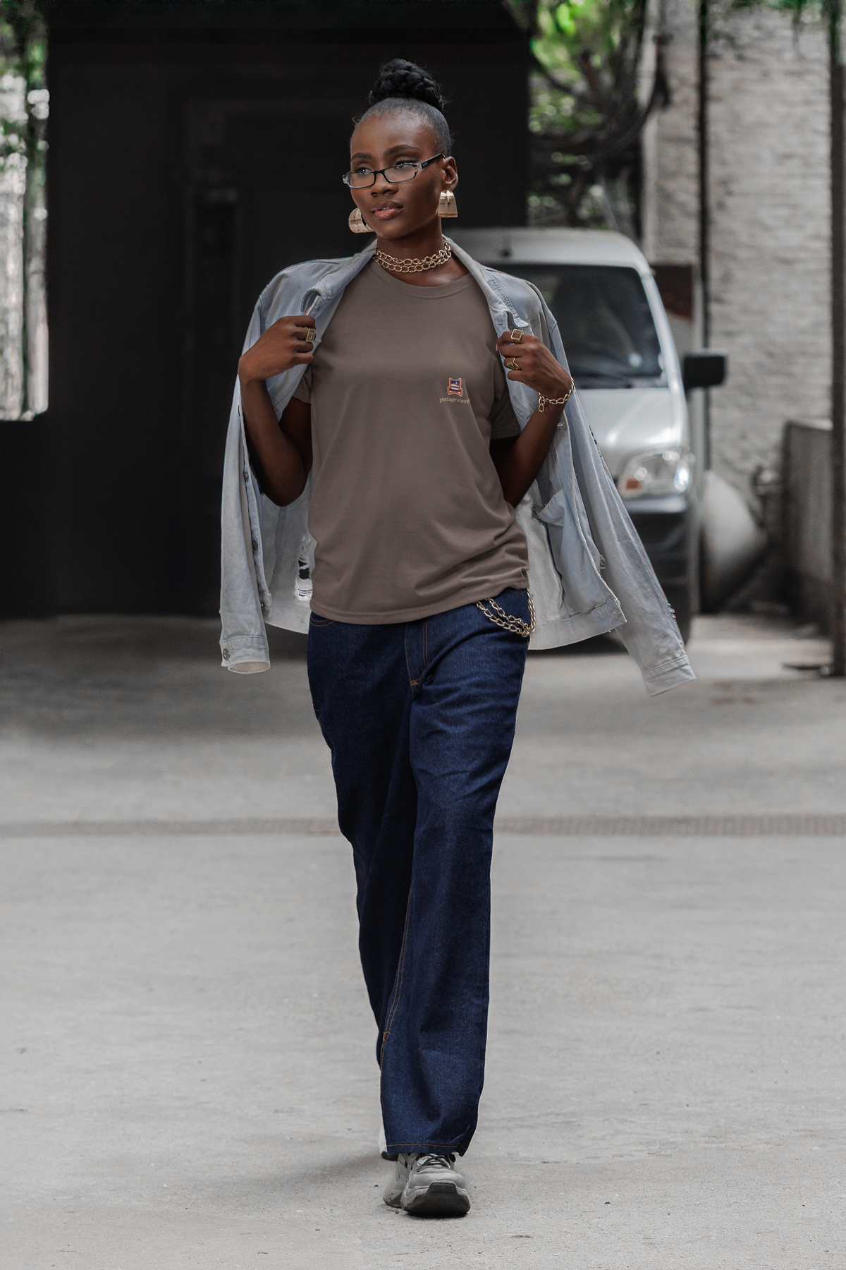 Edge of Evening Garment-Dyed Tee in Espresso, worn by a woman walking down a city street, with the Edge of Evening logo and portage.camp on the chest. Digital product mockup.
