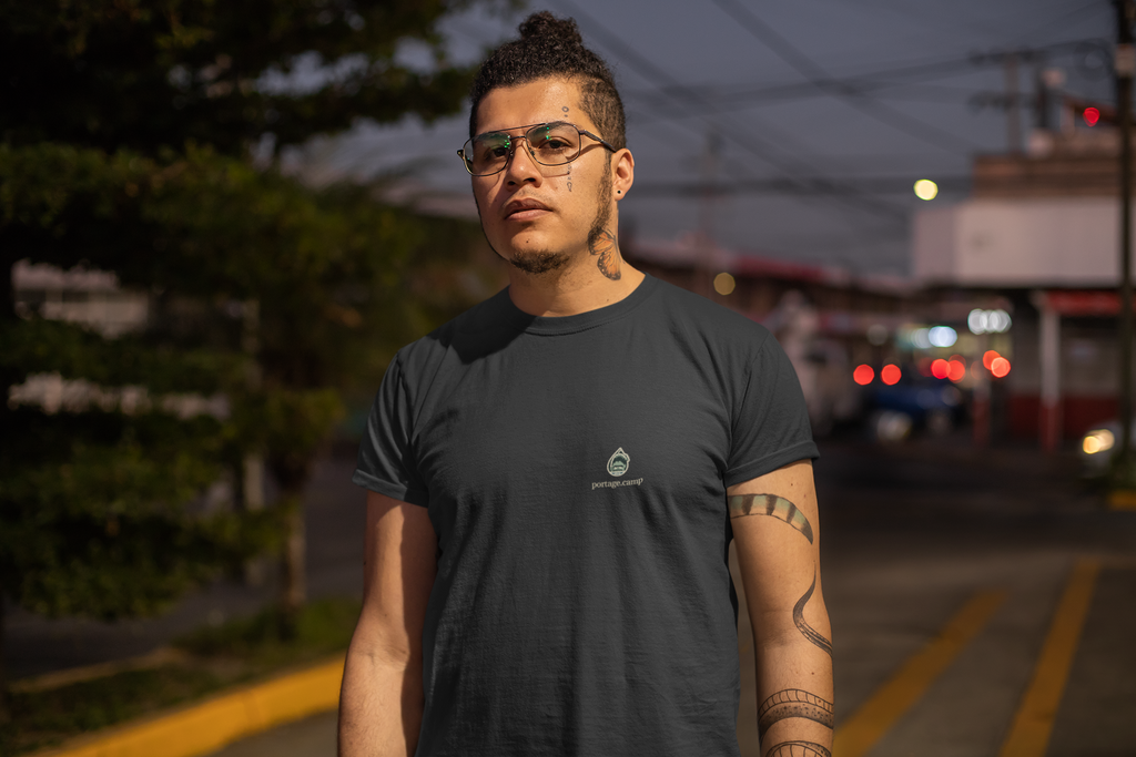 Rain Check Garment-Dyed Tee in Black, worn by a man on a street at dusk, with the Rain Check logo and portage.camp on the chest. Digital product mockup.