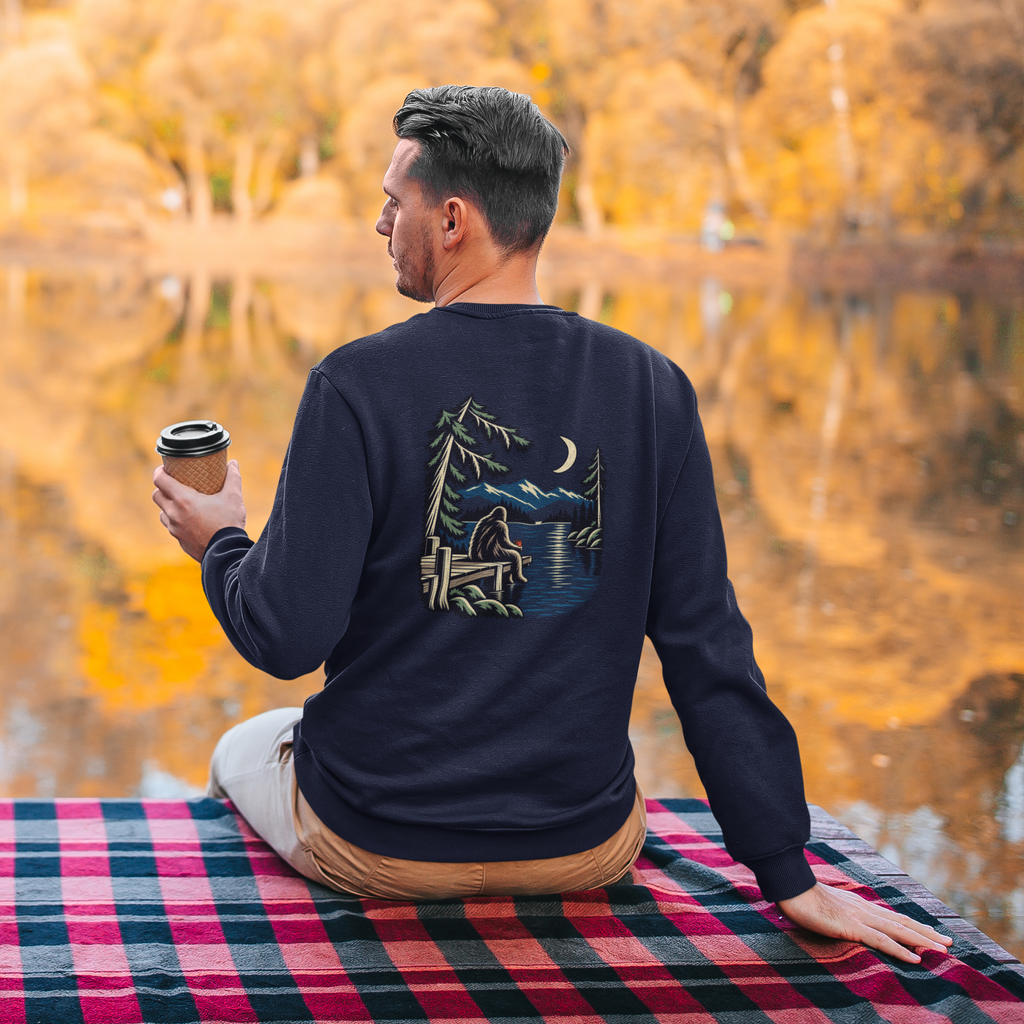 Quiet Hours Garment-Dyed Crewneck in True Navy, worn by a man seen from behind seated by a lake in autumn, showing the large print on the back. Digital product mockup.