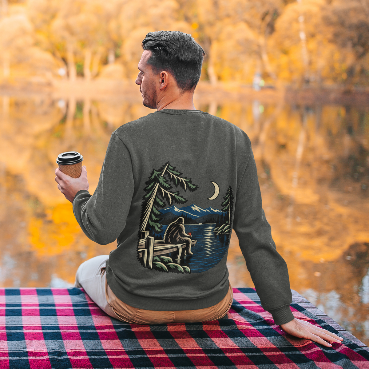 Quiet Hours Garment-Dyed Crewneck in Pepper, worn by a man seen from behind seated by a lake in autumn, showing the large print on the back. Digital product mockup.