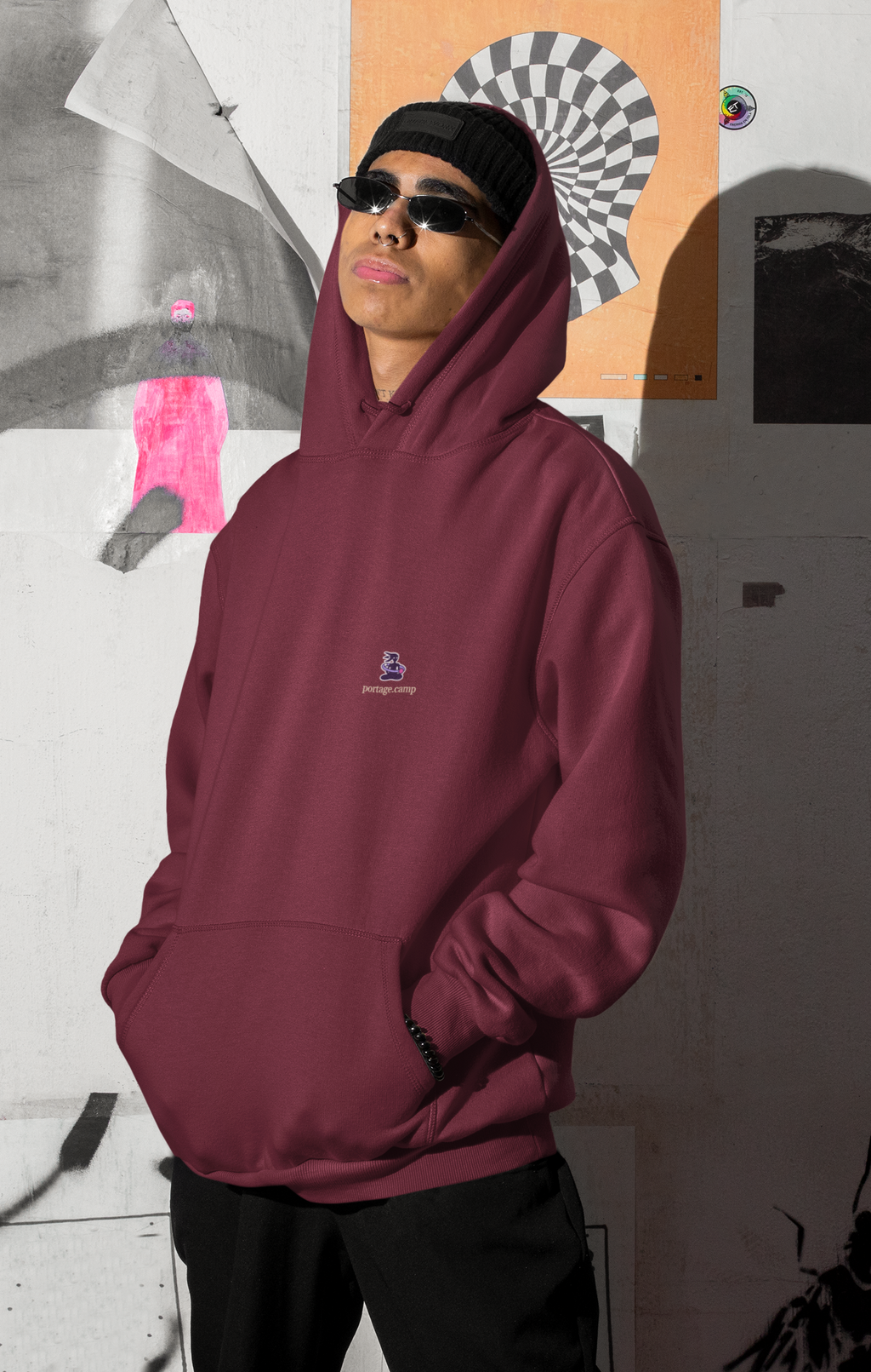 Orbit Keeper Midweight Hoodie in Maroon, worn by a man by a wall of posters, with the Orbit Keeper logo and portage.camp on the chest. Digital product mockup.
