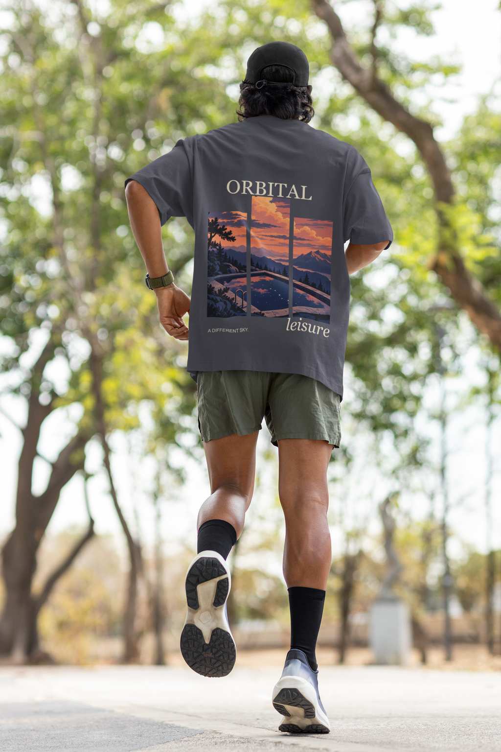 A Different Sky Garment-Dyed Tee in Navy, worn by a man seen from behind jogging through a park, showing the large print on the back. Digital product mockup.