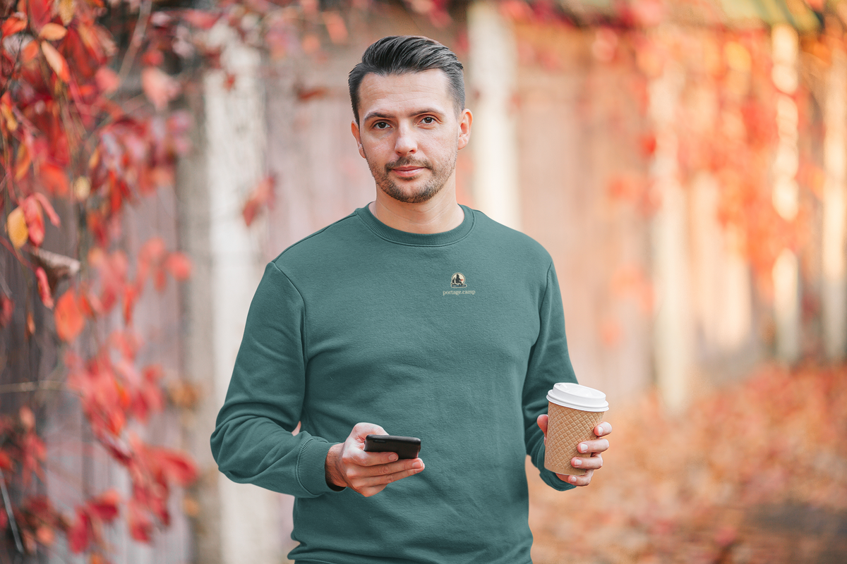 Quiet Hours Garment-Dyed Crewneck in Blue Spruce, worn by a man among autumn leaves, with the Quiet Hours logo and portage.camp on the chest. Digital product mockup.
