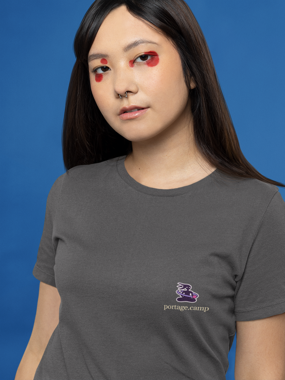 Orbit Keeper Garment-Dyed Tee in Graphite, worn by a woman with graphic eyeliner, close up, with the Orbit Keeper logo and portage.camp on the chest. Digital product mockup.