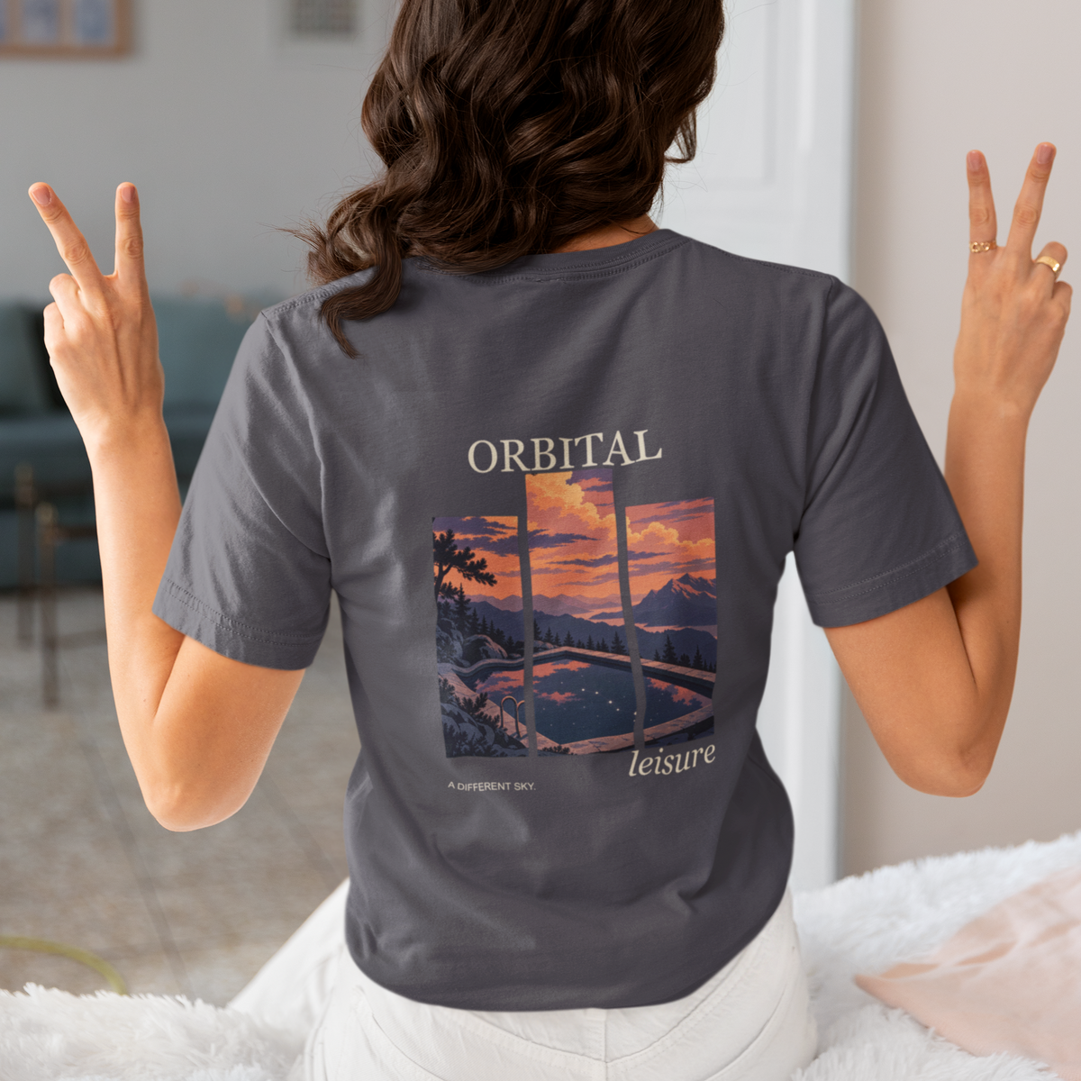 A Different Sky Garment-Dyed Tee in Navy, worn by a woman seen from behind making peace signs, showing the large print on the back. Digital product mockup.