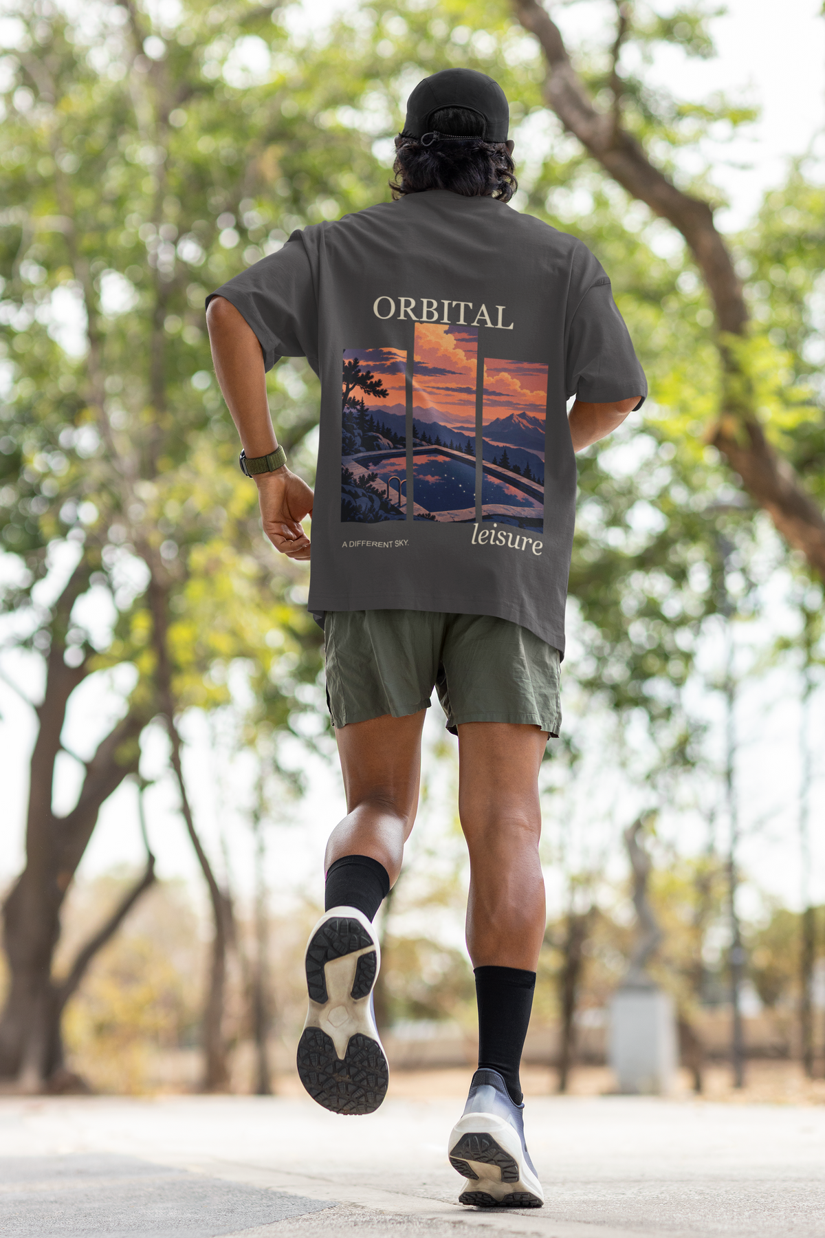 A Different Sky Garment-Dyed Tee in Graphite, worn by a man seen from behind jogging through a park, showing the large print on the back. Digital product mockup.