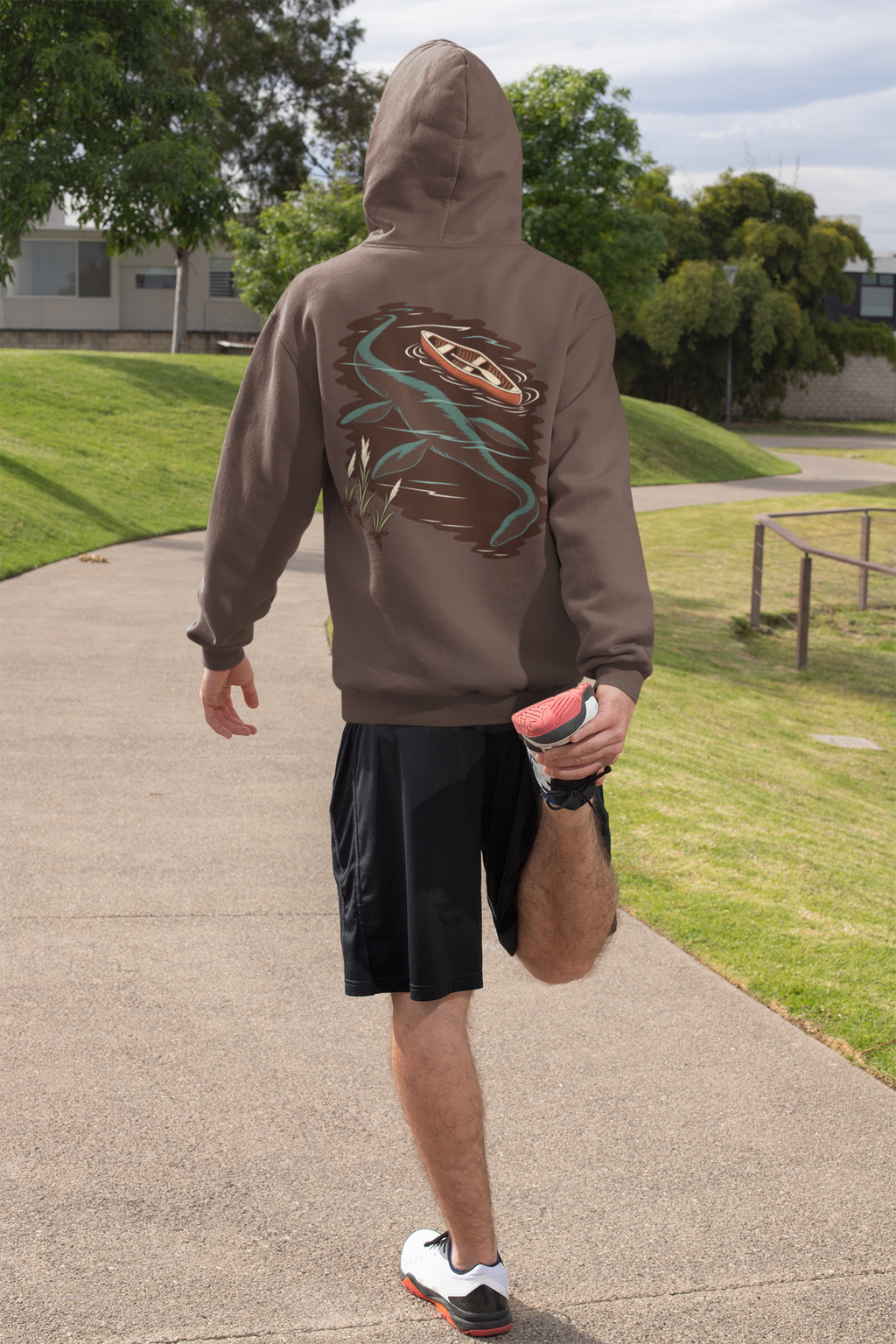 Seen Briefly Heavyweight Hoodie in Brown, worn by a man seen from behind on a sunny path, ready for a run, showing the large print on the back. Digital product mockup.