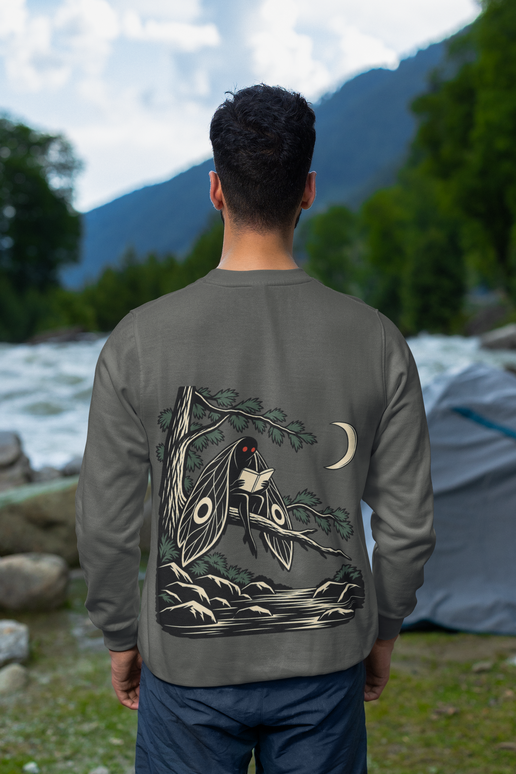 Night Library Garment-Dyed Crewneck in Pepper, worn by a man seen from behind looking out over a mountain valley, showing the large print on the back. Digital product mockup.
